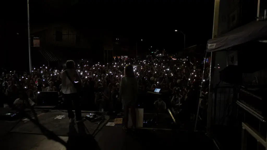 A nighttime crowd holds up illuminated phones during a performance at an outdoor music festival stage.