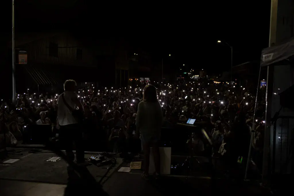 A large crowd holds up illuminated phones and devices during a nighttime concert performance at the Dancing Rabbit Music Festival.