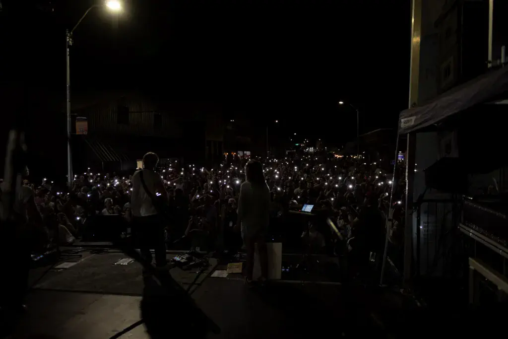 A nighttime concert with performers on stage and a large crowd holding up illuminated mobile phones.