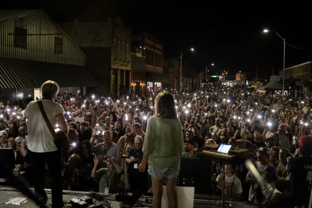 Night performance at an outdoor music festival with a large crowd holding up illuminated phones.