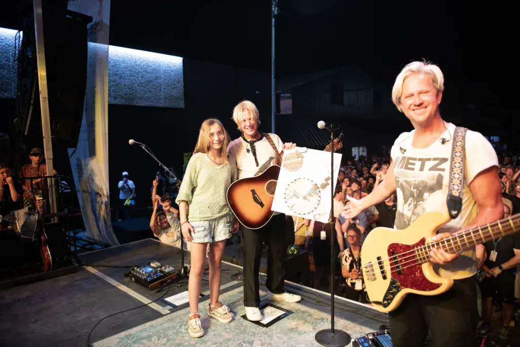 Band members perform on stage at Dancing Rabbit Music Festival with crowd watching from the sides.