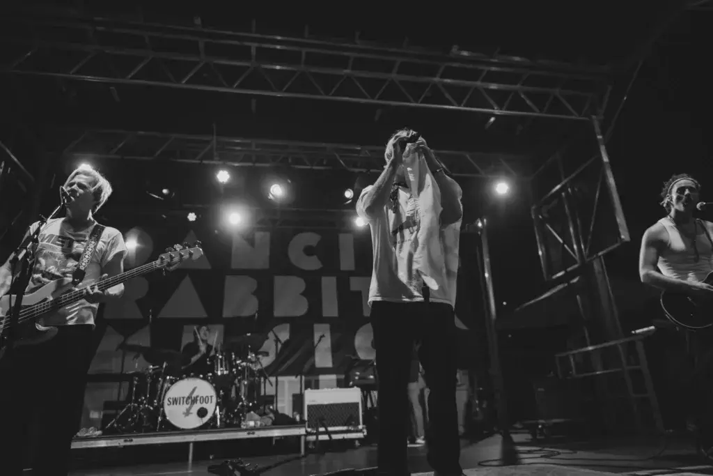 Black and white photograph of a live band performing on stage at Dancing Rabbit Music Festival with dramatic lighting.