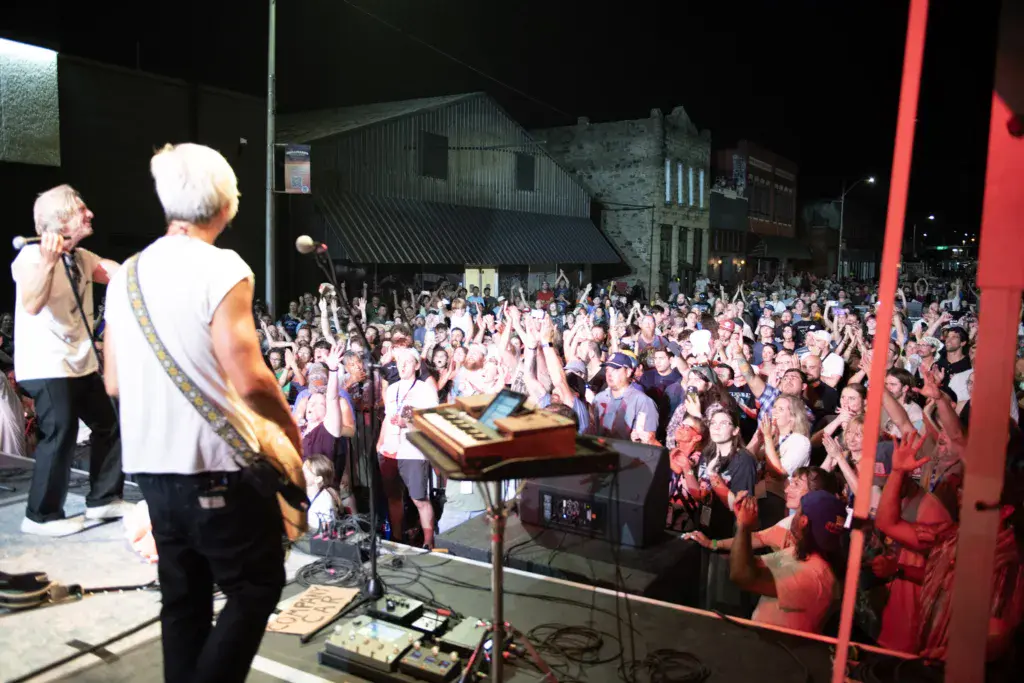 Musicians perform on an outdoor stage at night before a large crowd at Dancing Rabbit Music Festival.