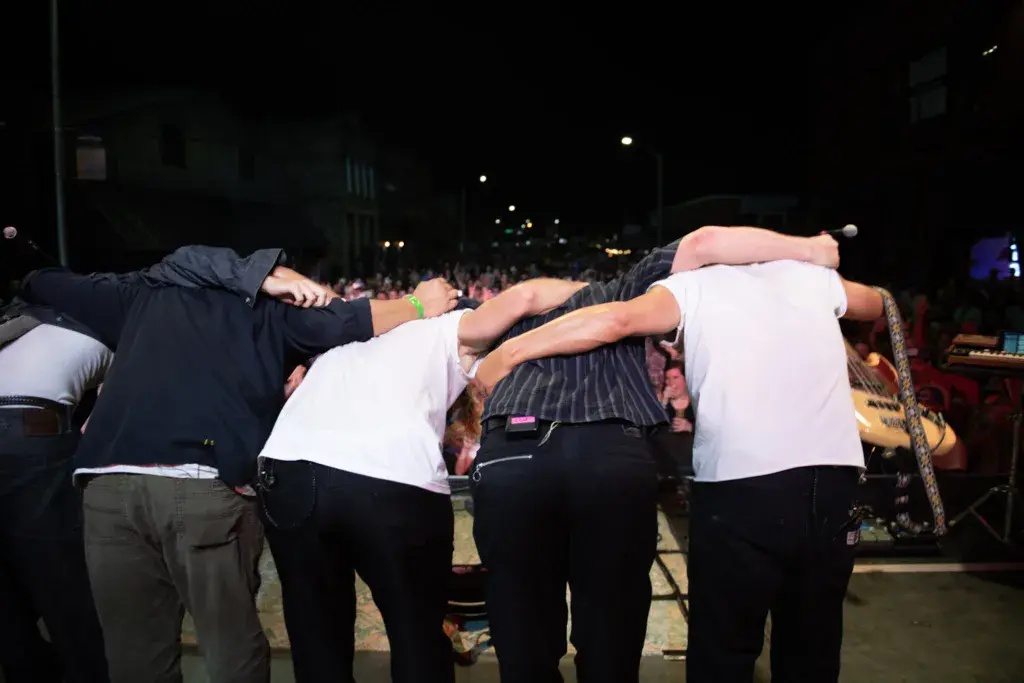 A group of people link arms on stage during a nighttime performance at the festival.